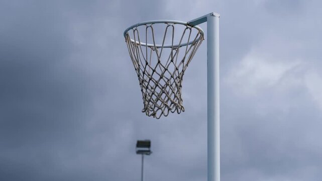 Outdoor netball goal and net in the wind against an overcast sky. Weather impact on community sports infrastructure, Melbourne, Australia.
