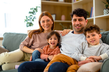 Obraz premium Happy family sitting together on sofa and smiling at camera