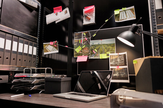 Empty dark police detective room with murder case investigation process on board. Suspect photographs connected with clues hanging on wall and file folders on racks in investigator agency office