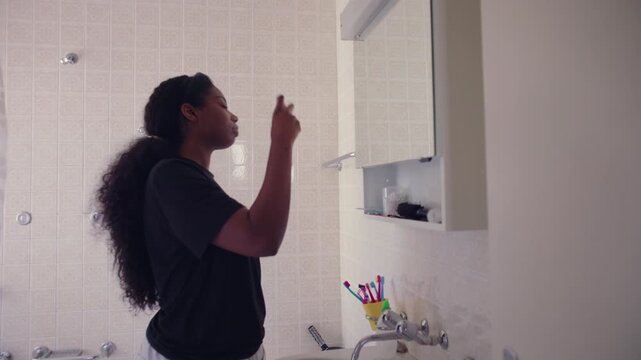 African American woman spraying facial mist while standing in bathroom with eyes closed creating refreshing and soothing beauty routine moment in calm home interior