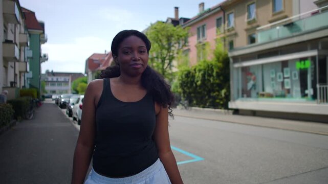 African American woman standing on residential street smiling toward camera creating warm and approachable urban lifestyle moment in everyday outdoor environment