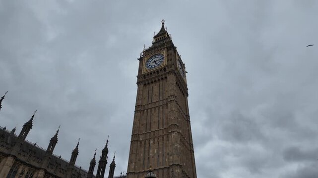 Dramatic low angle view of london's big ben clock tower rotating against a moody, overcast sky, showcasing its iconic gothic revival architecture and clock face