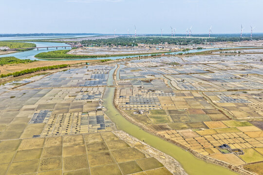 Aerial view of patchwork fields reflecting the sky's muted tones, divided by winding waterways leading to a distant bridge, Cox's Bazar, Chittagong Division, Bangladesh.