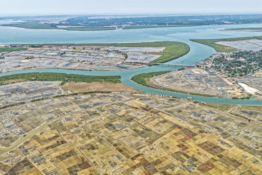 Aerial view of a river snaking through a landscape mosaic of salt pans and aquaculture farms under a vast sky, Cox's Bazar, Chittagong Division, Bangladesh.