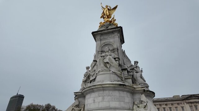 Queen victoria memorial statue with the winged victory sculpture gilded in gold, a london landmark in front of buckingham palace under a cloudy sky in england