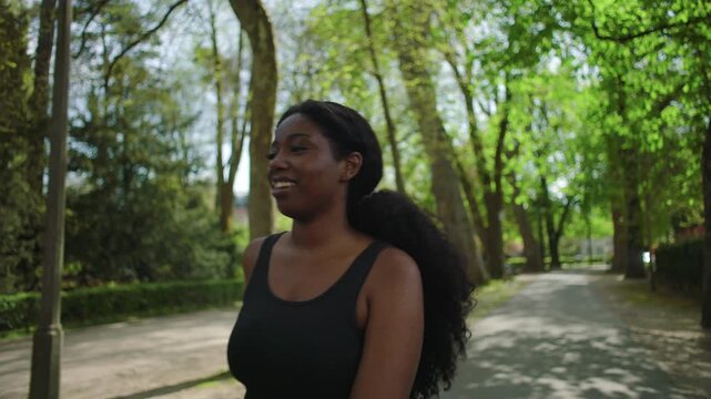 African American woman walking through park path while smiling and enjoying moment as camera follows her creating light and carefree outdoor lifestyle scene in nature