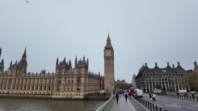 Famous london landmark, big ben and the houses of parliament, on a cloudy day with traffic crossing westminster bridge over the river thames