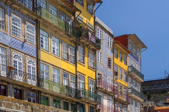 Aerial view of vibrant Ribeira houses with intricate blue tilework and colorful facades lining the Douro River under a clear sky, Porto, Porto District, Portugal.