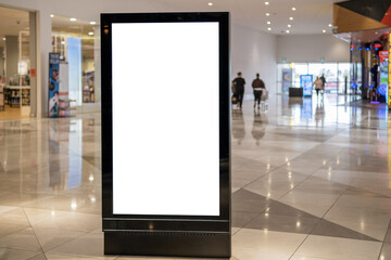 A blank white vertical digital billboard lightbox display stand mockup in a modern Australian shopping centre mall corridor, with blurred shoppers and retail stores in the background. Template for ads