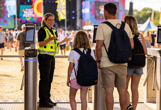 Smiling female security officer greeting a family at music festival entrance gates, event safety and crowd management for outdoor summer concert