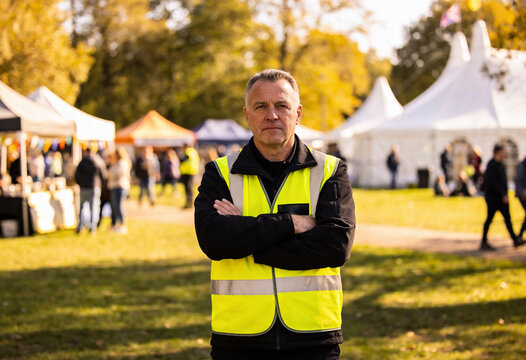 Mature male security staff standing with arms crossed at outdoor autumn festival, event management and crowd safety for public gathering and volunteer service