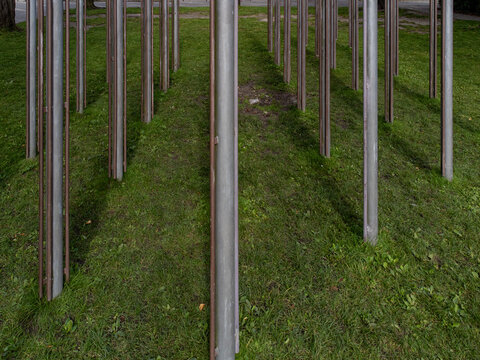 Aerial view of metallic pillars piercing through a carpet of vivid green grass, creating a stark contrast between industrial and natural elements, Almere, Flevoland, Netherlands.