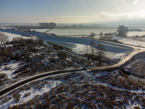 Aerial view of a snow-dusted landscape where the serene, frozen Vlietberg contrasts with the rugged textures of Tiengeboden, Ooij, Gelderland, Netherlands.