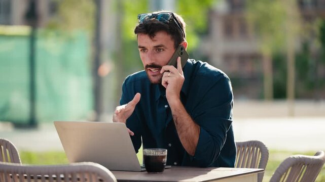 Video of happy businessman working with laptop while talking with smartphone having a drink on a terrace in the city