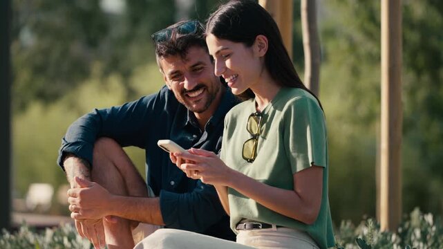 Video of lovely couple talking and laughing while looking together at smartphone in a park