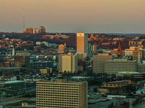 Aerial view of city buildings catching the warm glow of the setting sun, with UC Health and other landmarks visible in the distance, Cincinnati, Ohio, United States.