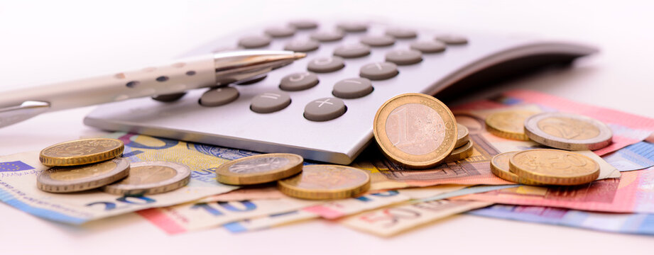 Unter einem Taschenrechner liegen viele Euro Banknoten und M&uuml;nzen
