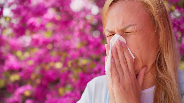 Woman suffering from pollen allergy in spring garden, sneezing with tissue. Seasonal allergy concept, health problem during blooming period outdoors.