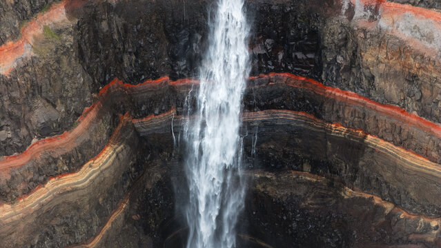 Aerial view of the Hengifoss waterfall cascading down the cliff's basalt layered rock face with striking red clay bands, Hengifoss, Iceland.