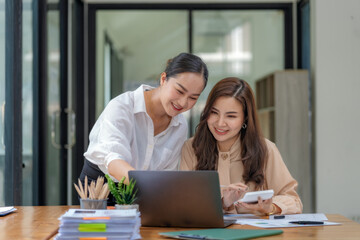 Fototapeta premium Two Asian businesswomen collaborating and discussing financial project on laptop and documents in office.