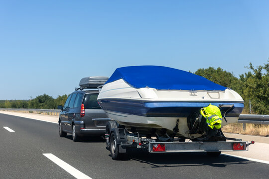 Family van towing covered boat trailer drives along empty highway clear blue sky surrounded by hills. Bright summer day creates sense freedom travel adventure mobile lifestyle on scenic route