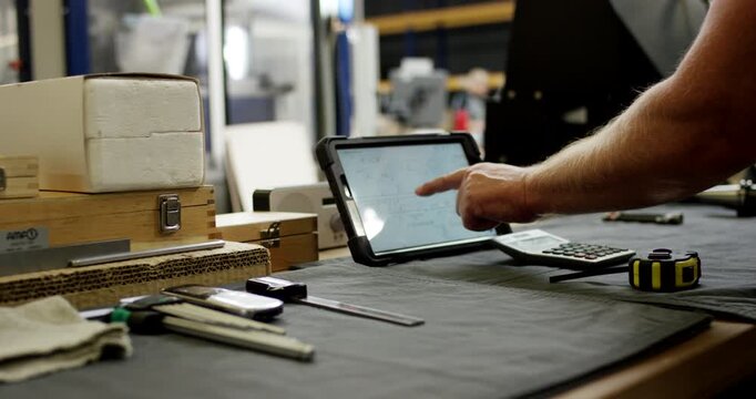 Hand of a technician using a digital tablet with technical drawings on a workbench in a workshop