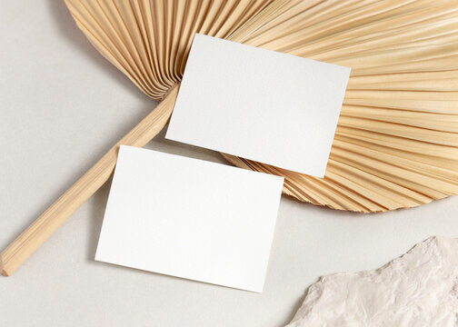 Blank sided cards set mockup with dried palm leaf on beige stone top view, wedding stationery