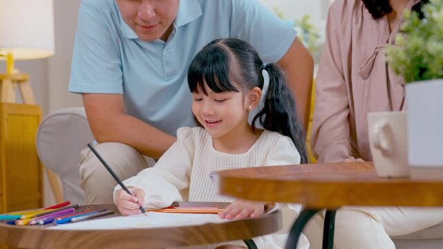 Asian family bonding as young daughter colors on paper with father and mother, encouraging creativity in their cozy living room.