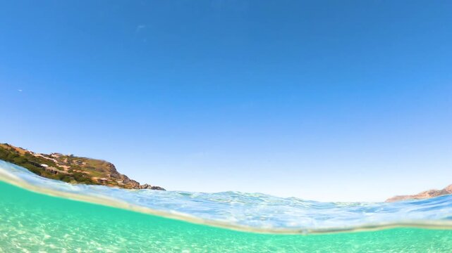 Split underwater view of La Pelosa beach in Stintino Sardinia with clear turquoise water and iconic tower visible in the background in slow motion