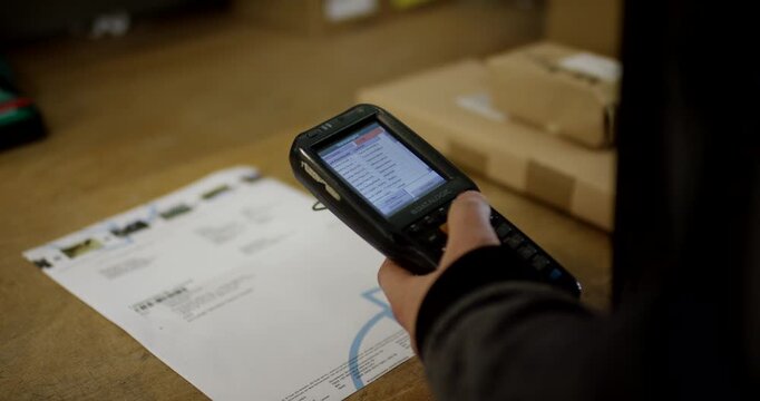 Technician using a handheld barcode scanner to check delivery documents and packages on a workbench