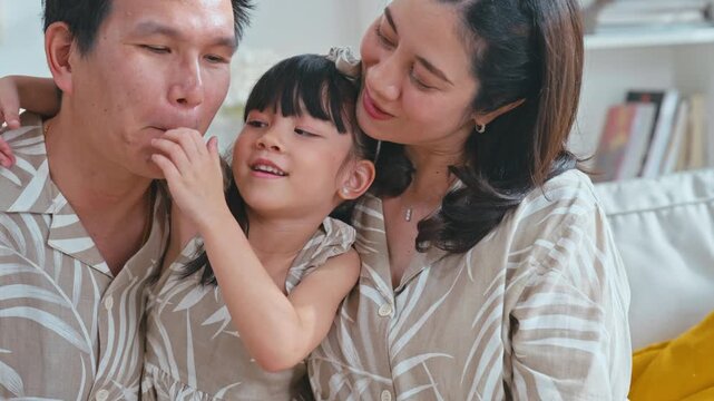 Slow motion Close-up portrait of happy Asian family father, mother, daughter smiling on living room sofa.