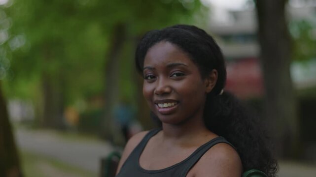 African American woman sitting on park bench looking toward camera with soft and friendly smile creating warm and approachable outdoor portrait moment in natural environment