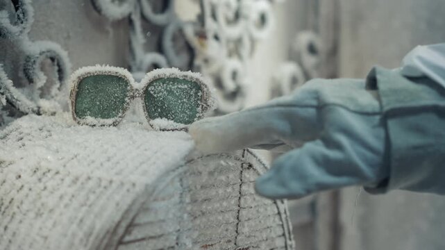 Frostcovered sunglasses on rusty mailbox, gloved hand reaches to touch, ornate iron fence backdrop, thick frost crystals coating lenses and post, quiet abandoned winter garden, eerie postapocalyptic