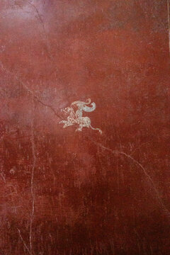Detail of a winged griffin fresco on a Pompeian red background in the Fullonica of Stephanus, Pompeii, Italy.