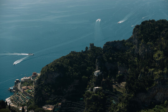 Aerial high angle view of boats leaving wakes in the blue sea along the rugged Amalfi Coast cliffs, Italy