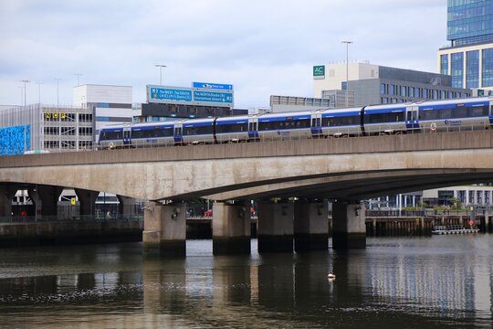 BELFAST, UK - JUNE 22, 2024: Translink NI Railways going over railway bridge over River Lagan against city skyline of Belfast, Northern Ireland.