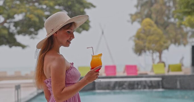 Smiling woman wearing straw hat holding colorful tropical cocktail, standing poolside at luxury beachfront resort, summer vacation travel marketing, luxury hospitality leisure background