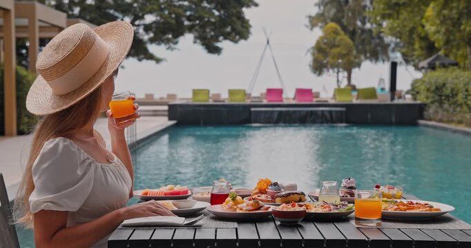 Young woman wearing straw hat drinking orange juice, luxury outdoor breakfast spread at tropical resort poolside, summer vacation lifestyle and high-end travel advertisement