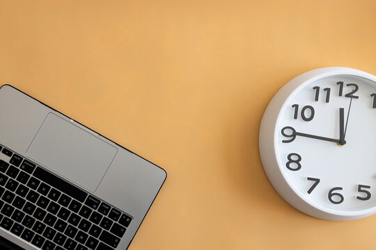 Laptop and wall clock on a beige background, symbolizing productivity, time management, remote work and modern workspace organization.