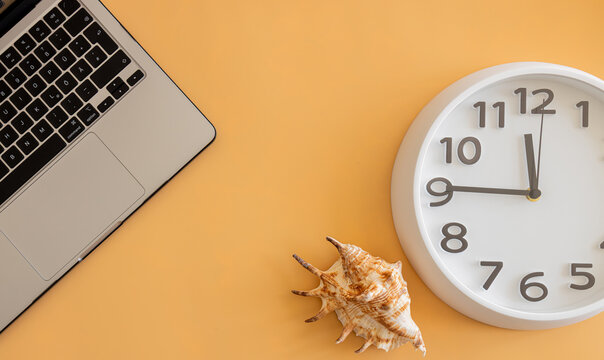 Flat lay with a laptop, wall clock and seashell on a pastel background, symbolizing work‑life balance, productivity, remote work and vacation planning.