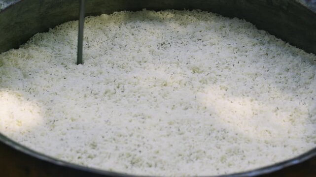 Chef making holes in rice with stick in large kazan for pilaf, close up