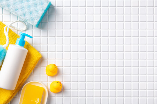 Yellow and blue bath accessories with soap and shampoo dispenser on white tile. Baby bathroom concept.