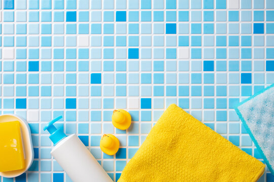 Baby cosmetic products, bath ducks, sponge and yellow towel on mosaic tiles background.