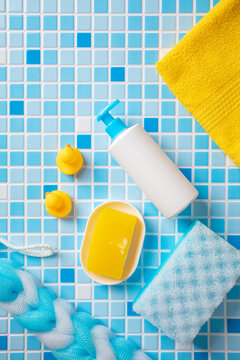 Baby bath products and yellow accessories for kids hygiene on blue and white tiles background. Top view, vertical