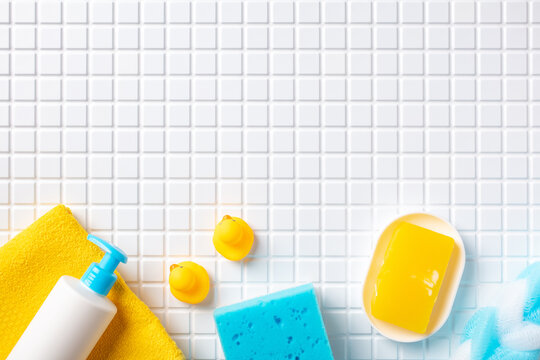 Set of baby hygiene bath products and yellow soap on white grid tile background with copy space.
