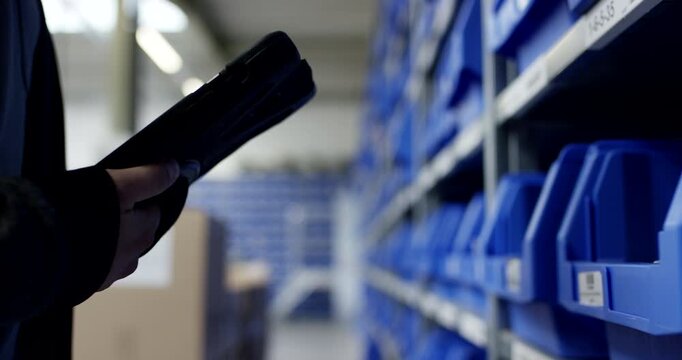 Warehouse worker using handheld terminal while picking parts from blue storage bins on shelving