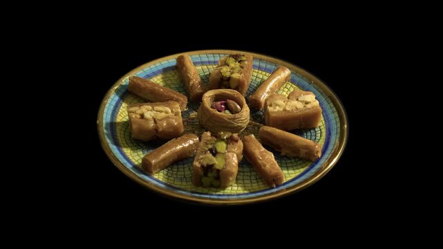 Gold-rimmed plate of baklava pastry dessert rotates on black background