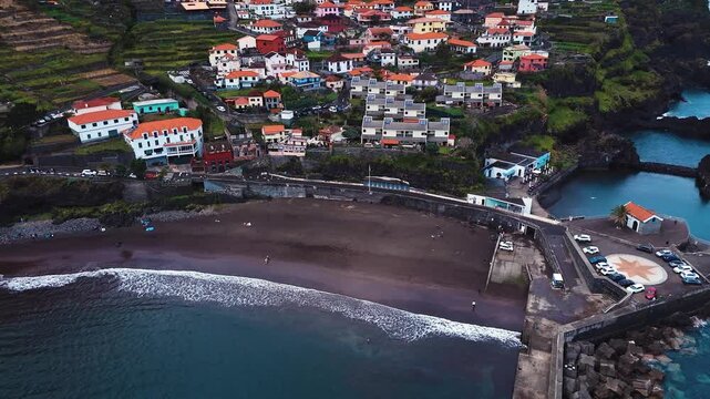 Aerial pan over Seixal beach, harbor and village with compass plaza