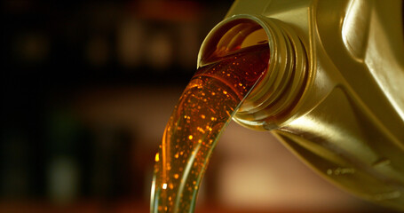 Close-up of motor oil pouring from a plastic container. Golden viscous liquid with bubbles flowing smoothly, automotive maintenance concept with shallow depth of field. © Jag_cz