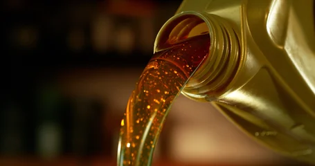 Close-up of motor oil pouring from a plastic container. Golden viscous liquid with bubbles flowing smoothly, automotive maintenance concept with shallow depth of field. © Jag_cz